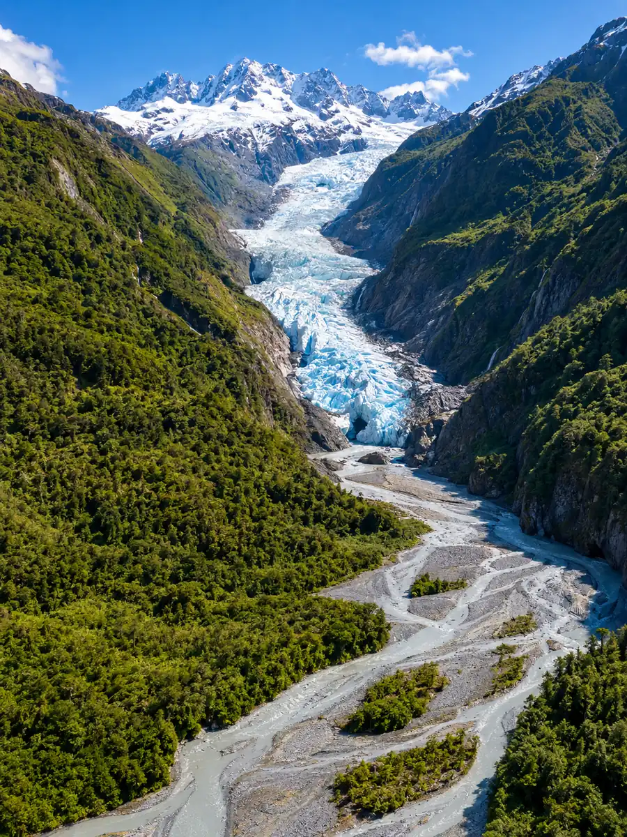 Luftaufnahme des Tals des Franz Josef Glacier, die Gletscherzunge zwischen Regenwaldwänden und ein verzweigter Fluss darunter