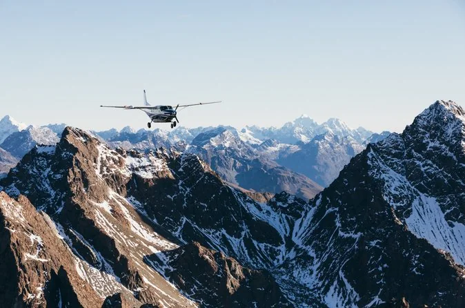 Ein kleines Flugzeug fliegt zwischen schroffen, verschneiten Gipfeln