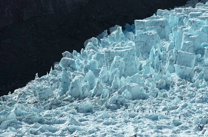 Die zerklüfteten blauen Séracs des Eisbruchs am Franz Josef mit einer Reihe winziger Wanderer unten