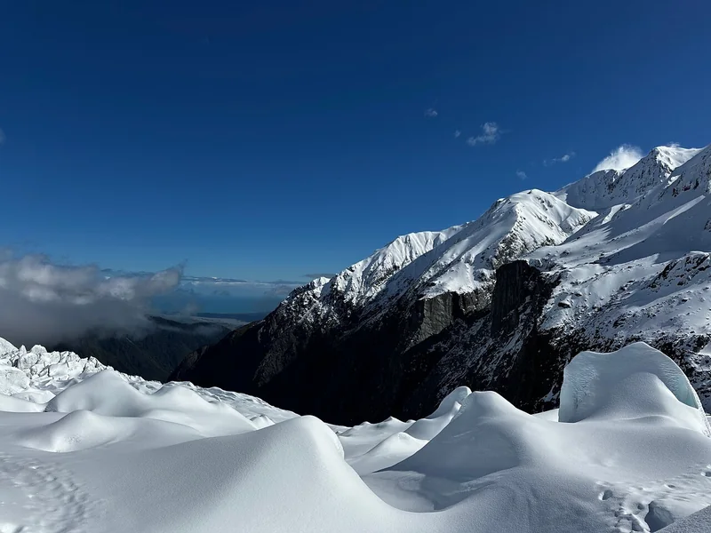 A bright sunlit snowfield on the glacier under deep blue sky with mountains behind