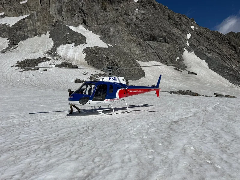 A helicopter parked on a snowfield below dark rock peaks