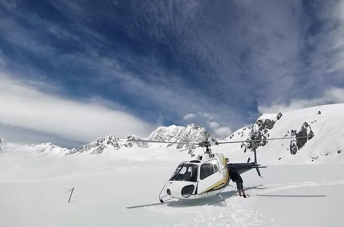 Ein Hubschrauber gelandet auf einem weiten Schneefeld unter bewölktem Himmel mit Gipfeln dahinter