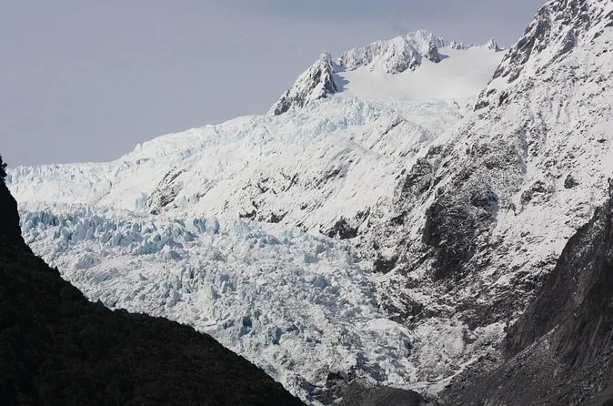 The white tongue of Franz Josef Glacier between dark rock walls and snowy peaks